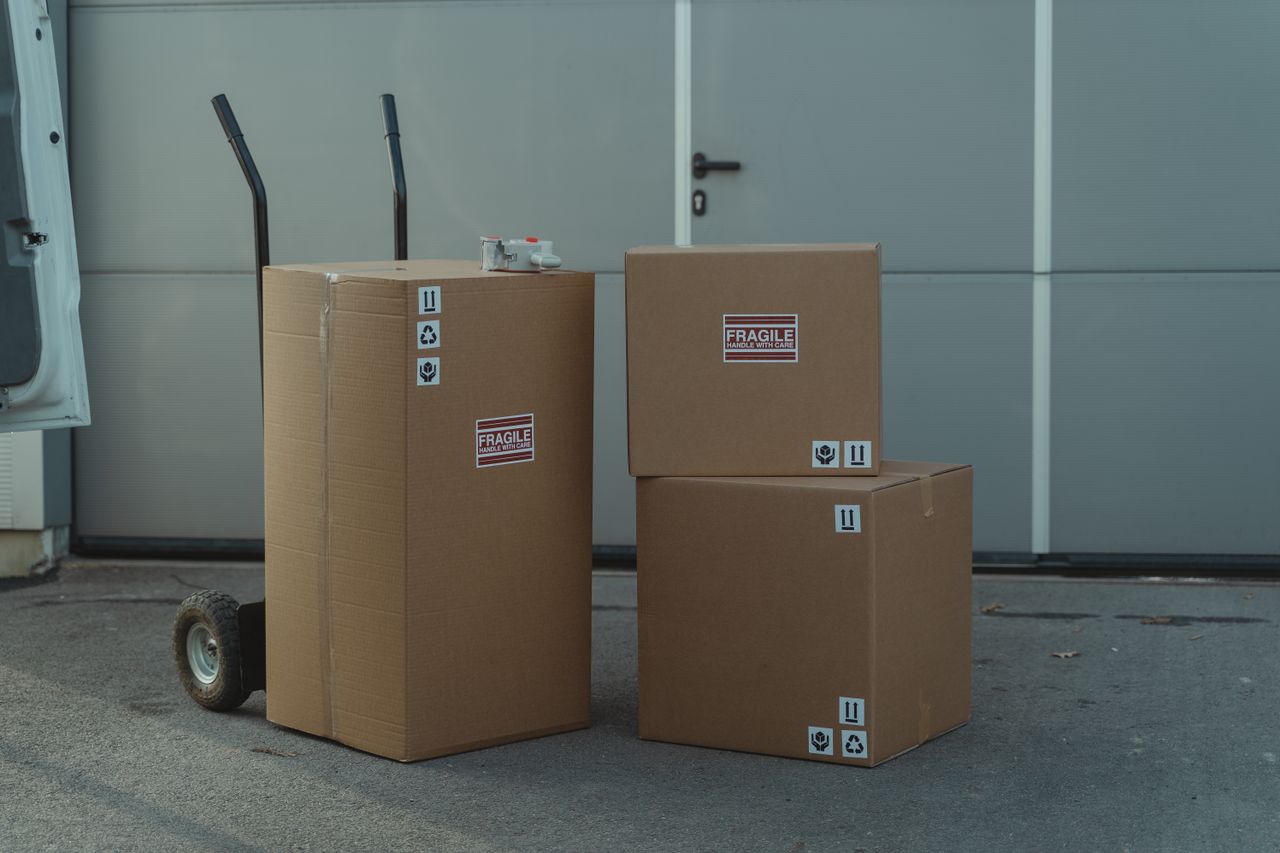 Three cardboard boxes on a dolly, ready for shipping outside a warehouse.