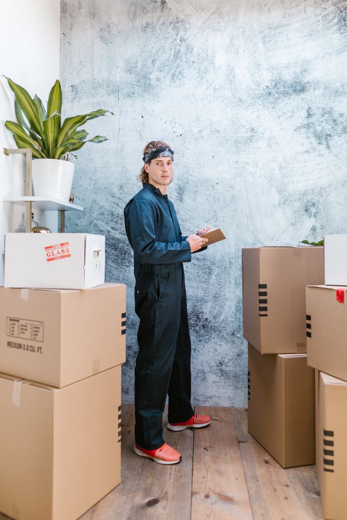 who-we-are A mover in coveralls with bandana checks packages in a warehouse.