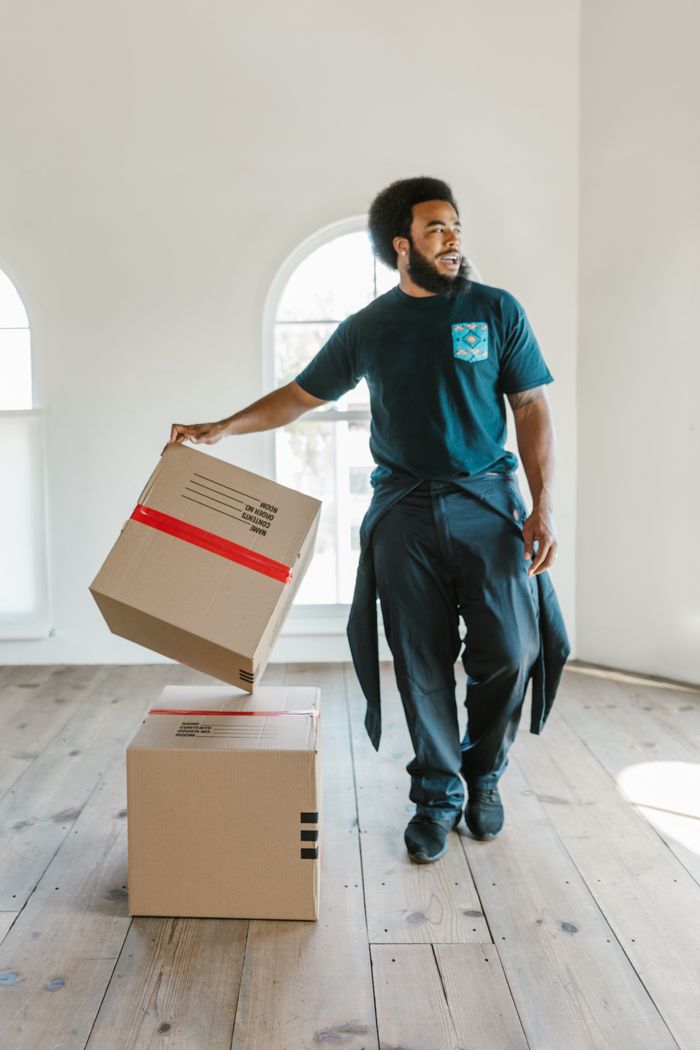 About A mover carefully handles boxes in a bright, empty room on moving day.
